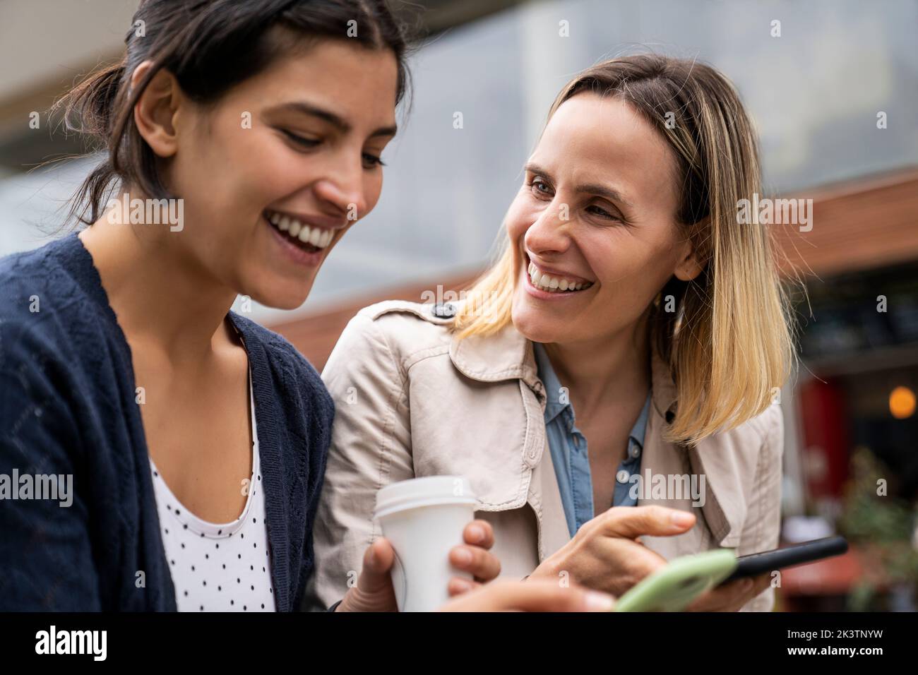 Flache Seitenansicht von zwei Freiberuflerinnen, die im Freien arbeiten und sich beim Prüfen ihrer Smartphones Vergnügen Stockfoto