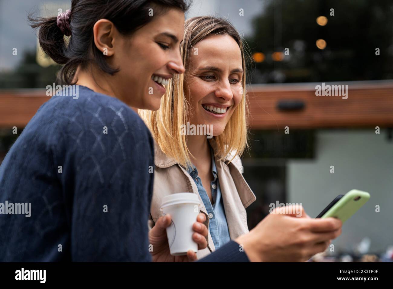 Mid-Shot-Seitenansicht von zwei Unternehmerinnen, die Nachrichten von ihren Followern auf ihren Smartphones überprüfen Stockfoto