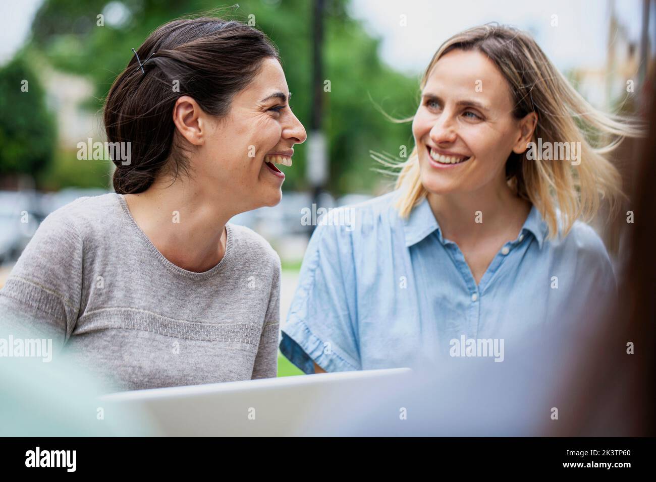 Weibliche Kollegen lachen, während sie draußen sitzen Stockfoto