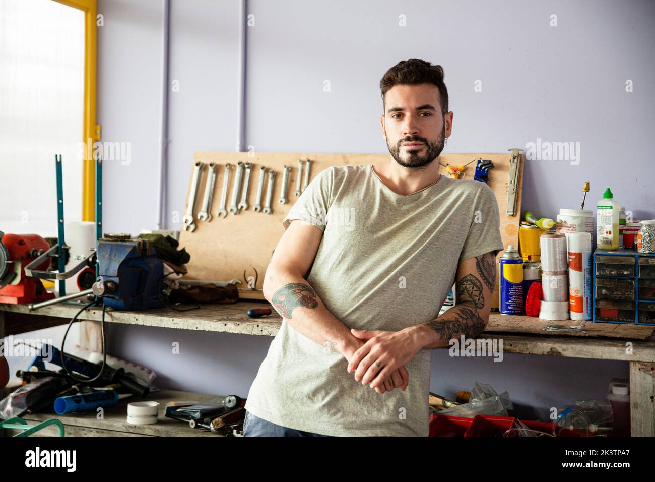 Junger erwachsener Mann, der sich auf die Werkbank lehnte, während er auf die Kamera schaute Stockfoto