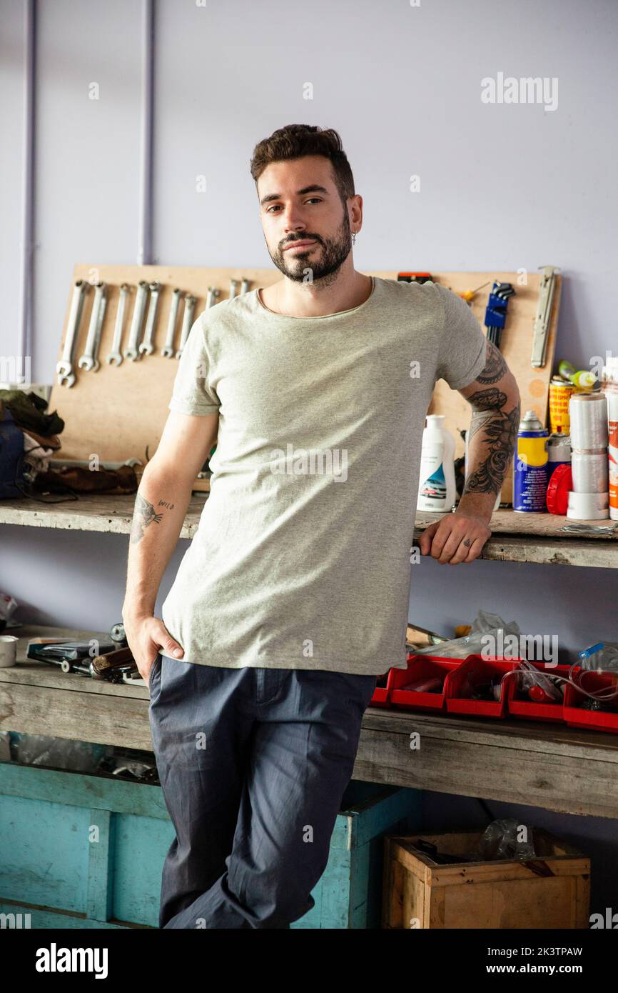 Junger erwachsener männlicher Mechaniker, der sich auf die Werkbank lehnt Stockfoto