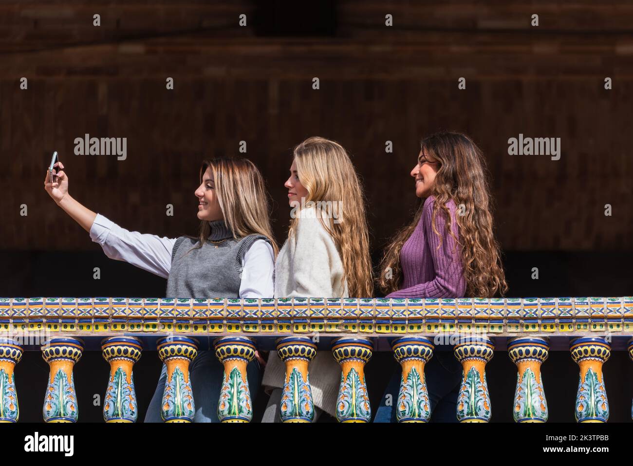 Flache Seitenansicht einer Gruppe von freundlichen Frauen, die am Wochenende in Sevilla auf dem Balkon auf der Plaza de Espana stehen und sich selbst auf dem Smartphone geschossen haben Stockfoto