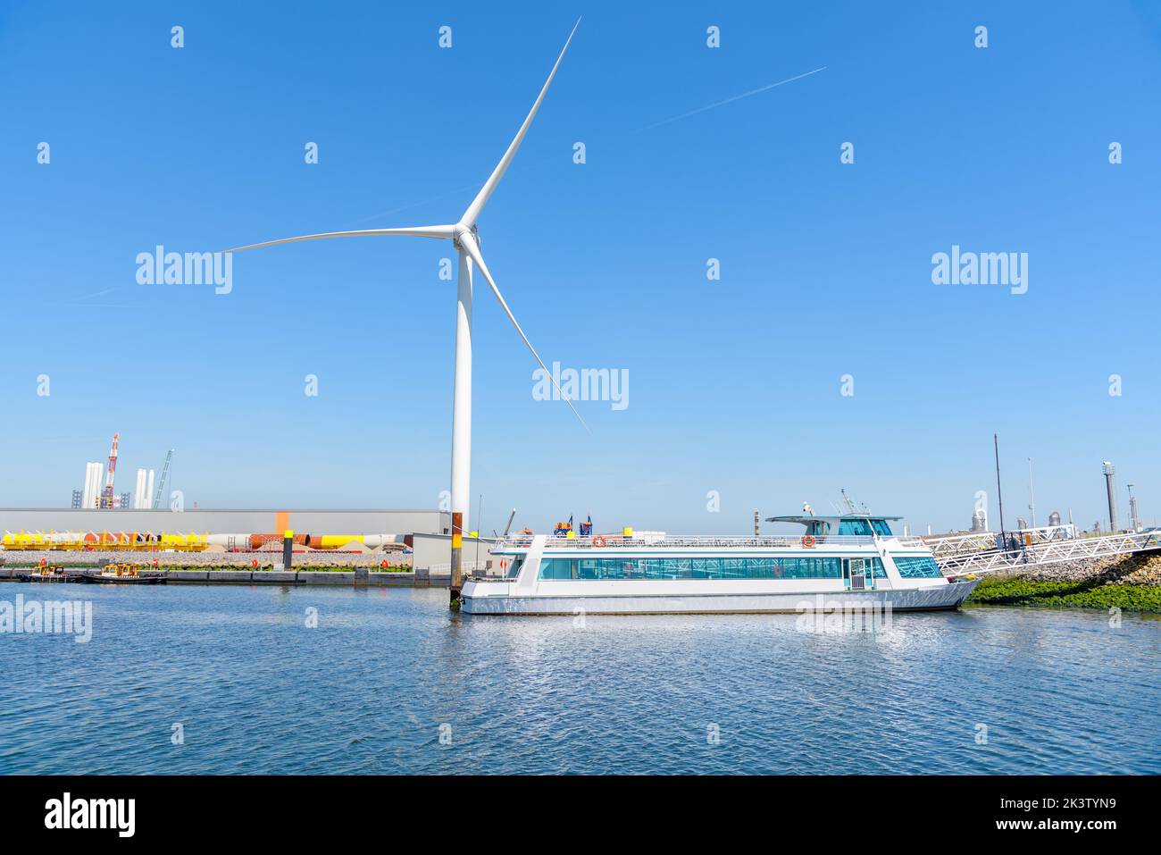 Leere Passagierfähre, die in einem Handelshafen mit einer hohen Windturbine im Hintergrund unter klarem Himmel vertäut ist Stockfoto