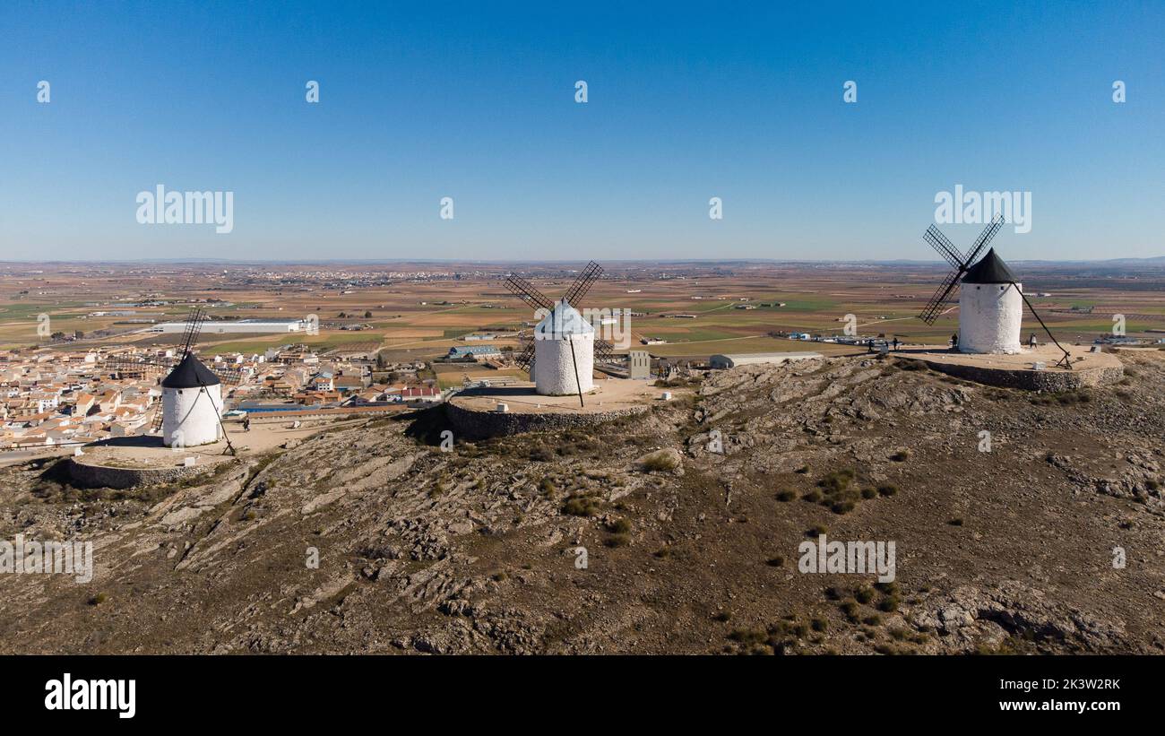 Weiße Windmühlen mit Klingen am Hang über der Stadt mit Wohnhäusern gegen den blauen Himmel in Consuegra an sonnigen Tagen Stockfoto