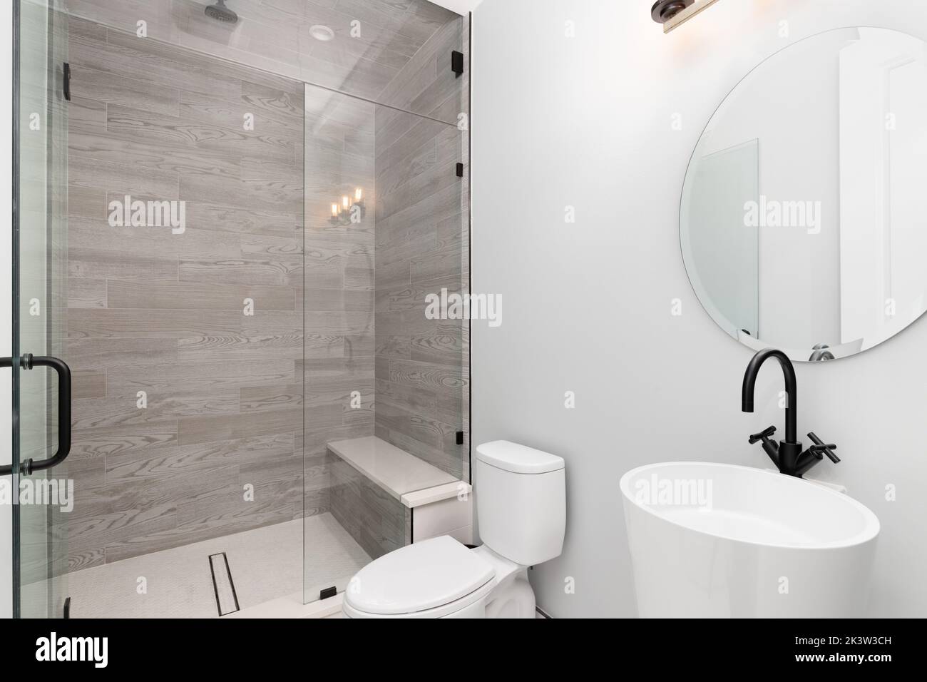 Luxuriöses Badezimmer mit rundem Spiegel, Dusche mit Marmorfliesen und schwarzem Wasserhahn. Stockfoto