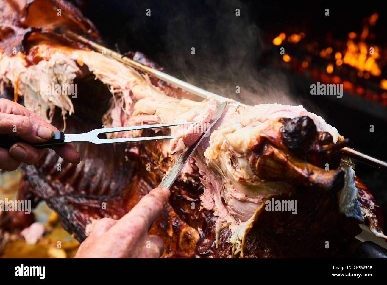 Der Koch schneidet das ganze gegrillte Schweinefleisch für Steaks mit einem Messer. Vom Schwein gegrillte traditionelle Kohle und Feuer. Das kleine Ferkel wird ganz auf einem offenen Feuer geröstet Stockfoto