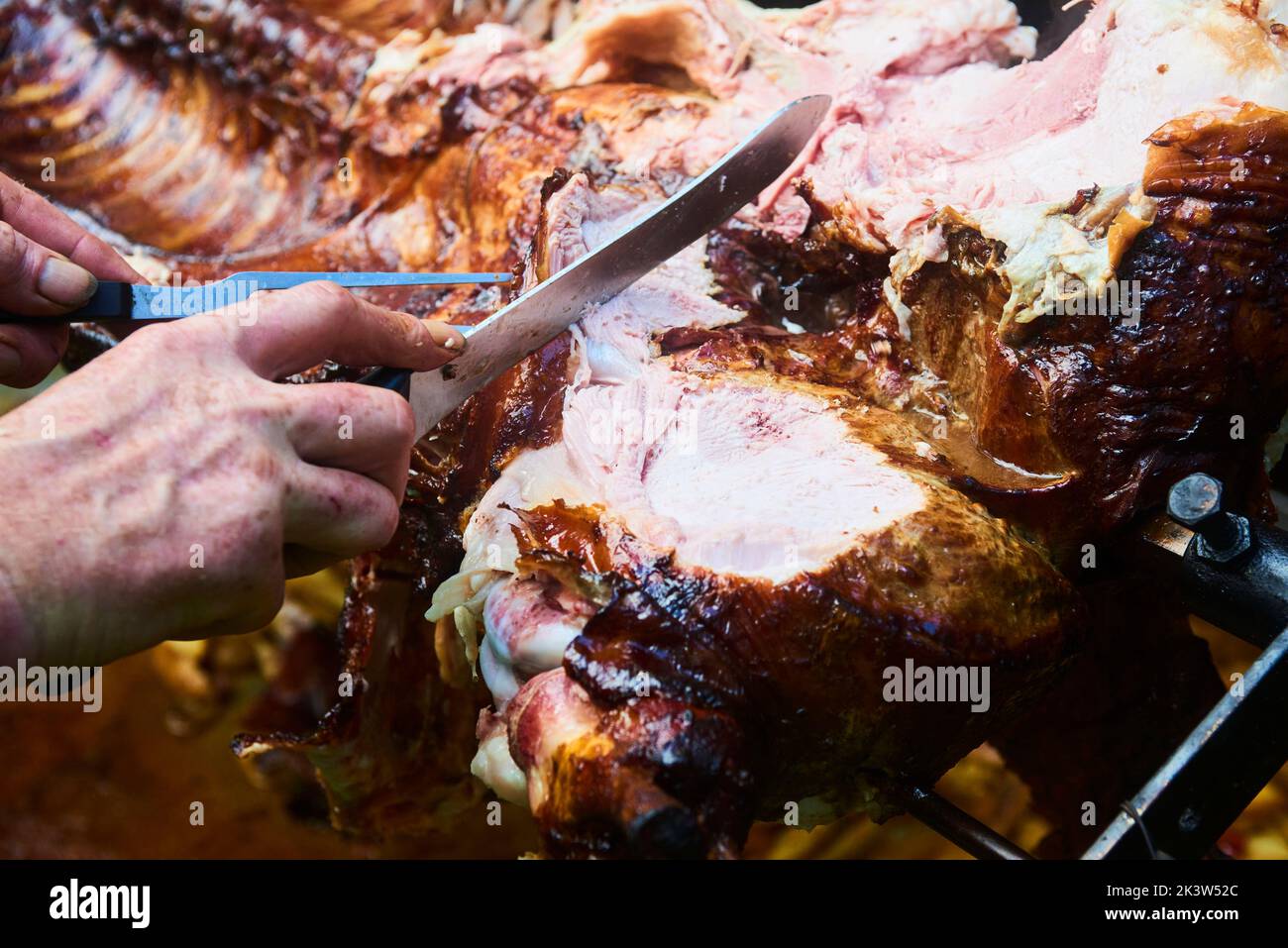 Der Koch schneidet das ganze gegrillte Schweinefleisch für Steaks mit einem Messer. Vom Schwein gegrillte traditionelle Kohle und Feuer. Das kleine Ferkel wird ganz auf einem offenen Feuer geröstet Stockfoto