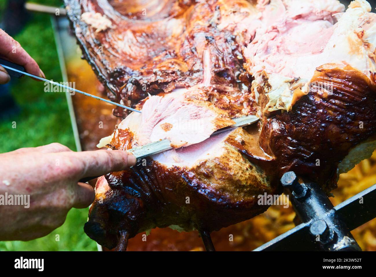 Der Koch schneidet das ganze gegrillte Schweinefleisch für Steaks mit einem Messer. Vom Schwein gegrillte traditionelle Kohle und Feuer. Das kleine Ferkel wird ganz auf einem offenen Feuer geröstet Stockfoto