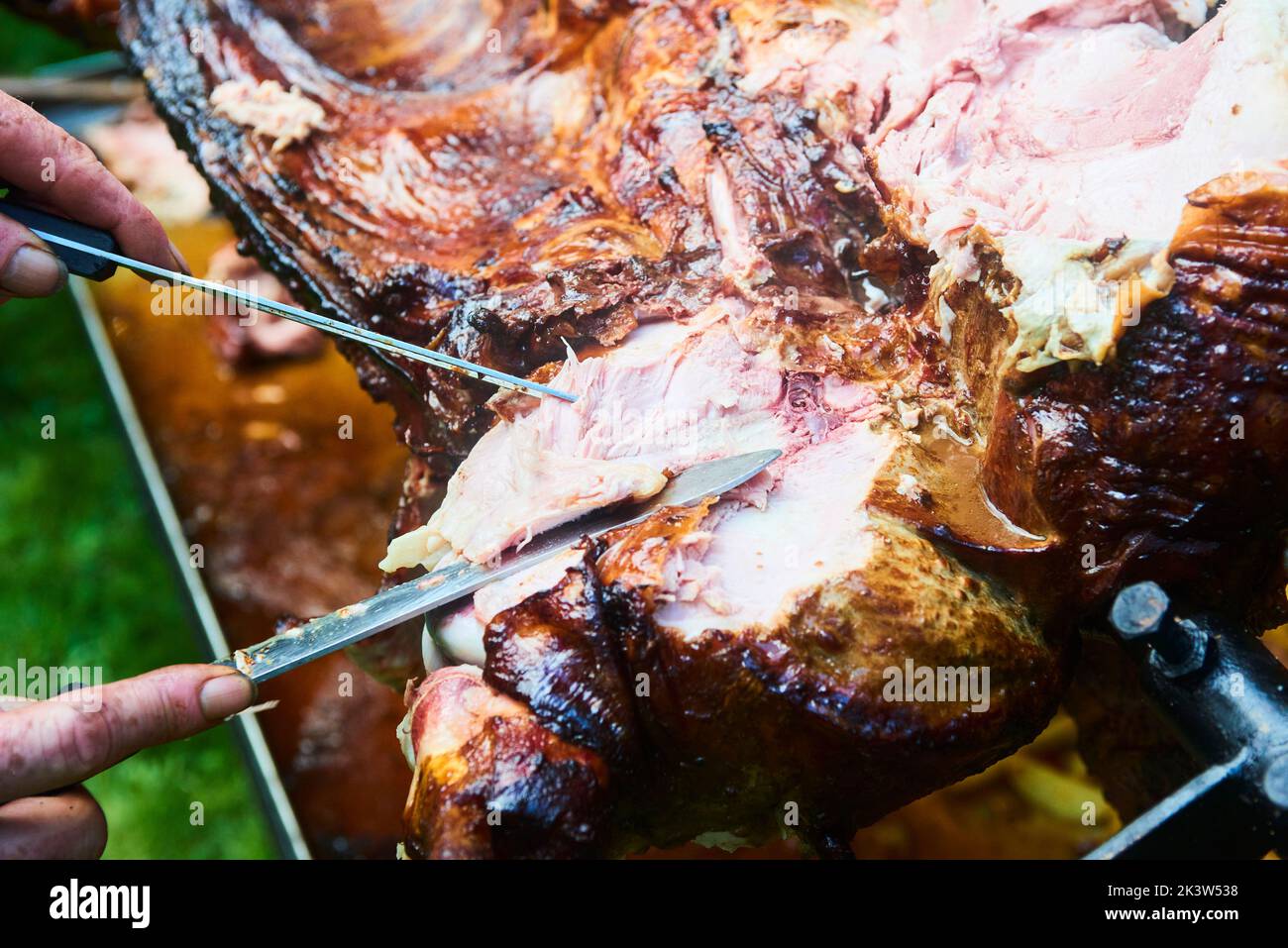 Der Koch schneidet das ganze gegrillte Schweinefleisch für Steaks mit einem Messer. Vom Schwein gegrillte traditionelle Kohle und Feuer. Das kleine Ferkel wird ganz auf einem offenen Feuer geröstet Stockfoto