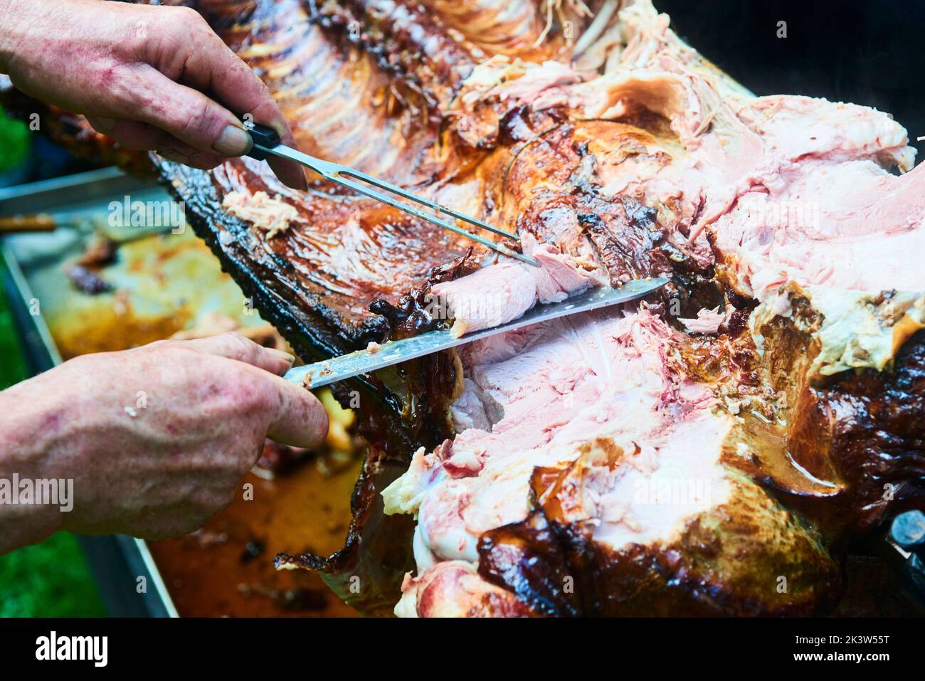 Der Koch schneidet das ganze gegrillte Schweinefleisch für Steaks mit einem Messer. Vom Schwein gegrillte traditionelle Kohle und Feuer. Das kleine Ferkel wird ganz auf einem offenen Feuer geröstet Stockfoto