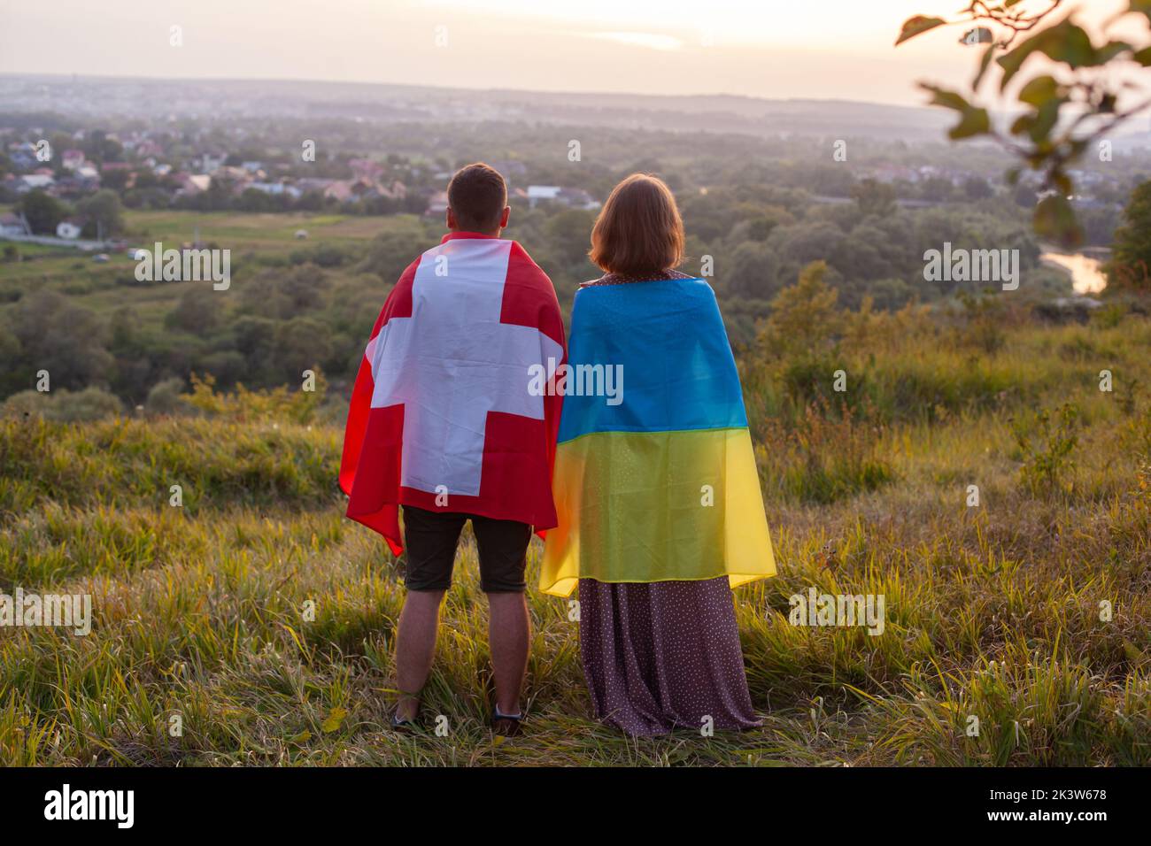 Paar bedeckt in Ukraine und Schweiz Flaggen. Konzept der Freundschaft zwischen der Ukraine und der Schweizerischen Eidgenossenschaft. Liebe zwischen zwei Ländern. Man und wo Stockfoto