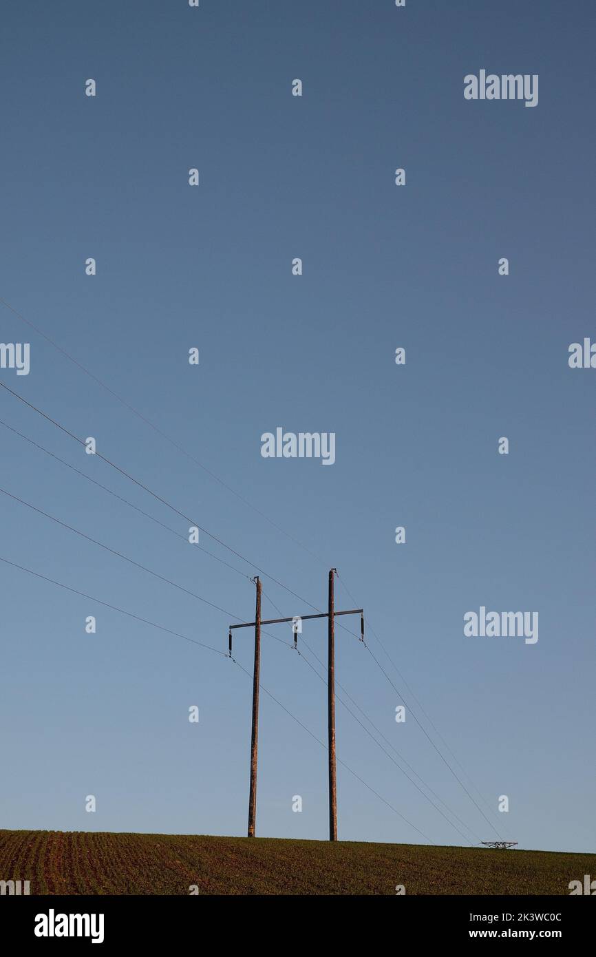 Eine vertikale Ansicht eines Telefonmastes in einem gepflügten Feld vor einem blauen Himmel Stockfoto