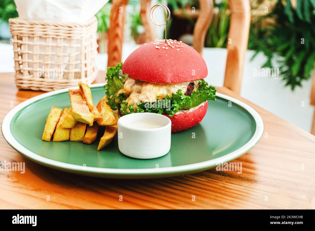 Veganer Burger, in einem roten Brötchen, Gericht mit Chips, auf einem grünen Teller, auf einem Holztisch, gesundes vegetarisches Essen. Stockfoto