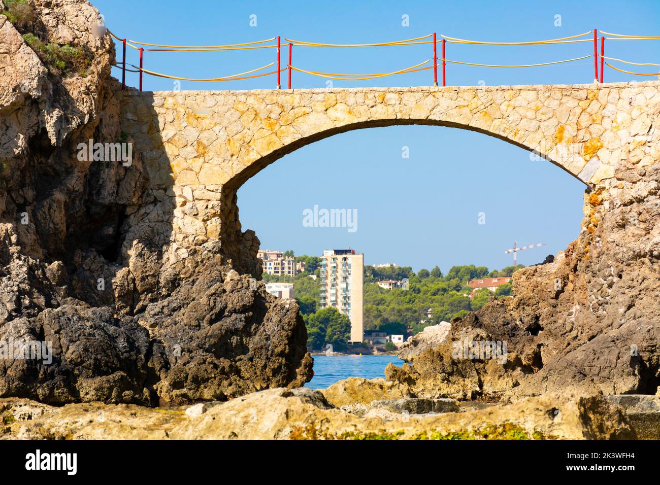 Palma, Mallorca, Spanien. Es Pujolar am Strand von Cala Major, eine kleine Brücke zu einer kleinen Insel in der Nähe der Küste. Im Hintergrund die Stadt Cas Catala oder S Stockfoto