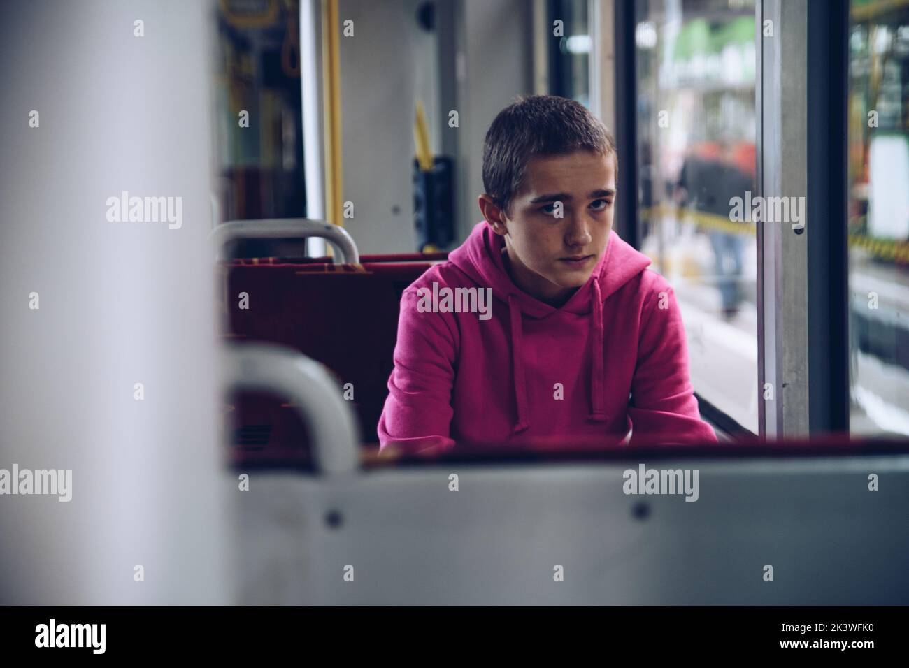 Teenager-Junge in einem rosa Kapuzenpullover, nachdenklich mit dem Bus unterwegs Stockfoto