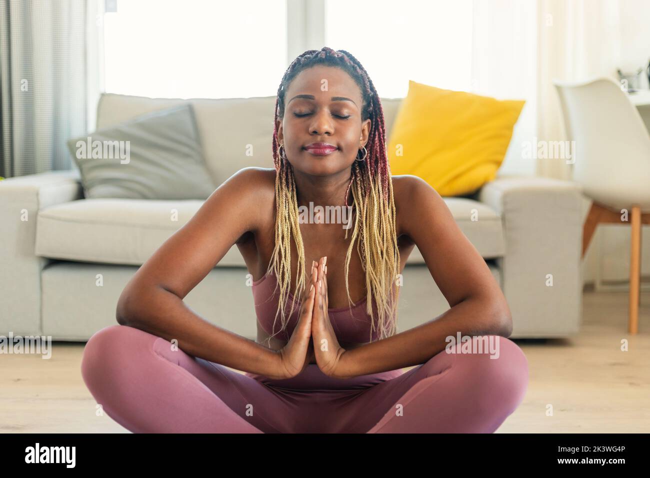 Friedliche schwarze Dame, die in Lotuspose sitzt, mit geschlossenen Augen meditiert und zu Hause auf der Yogamatte inneren Frieden erreicht Stockfoto