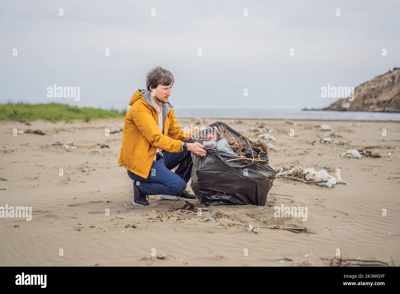 Plastikmüll. Meer- und Meeresverschmutzung. Strand sauber machen. Junger Mann pflückt gebrauchte Plastikflaschen am Sandufer. Sammeln von Umweltaktivisten Stockfoto