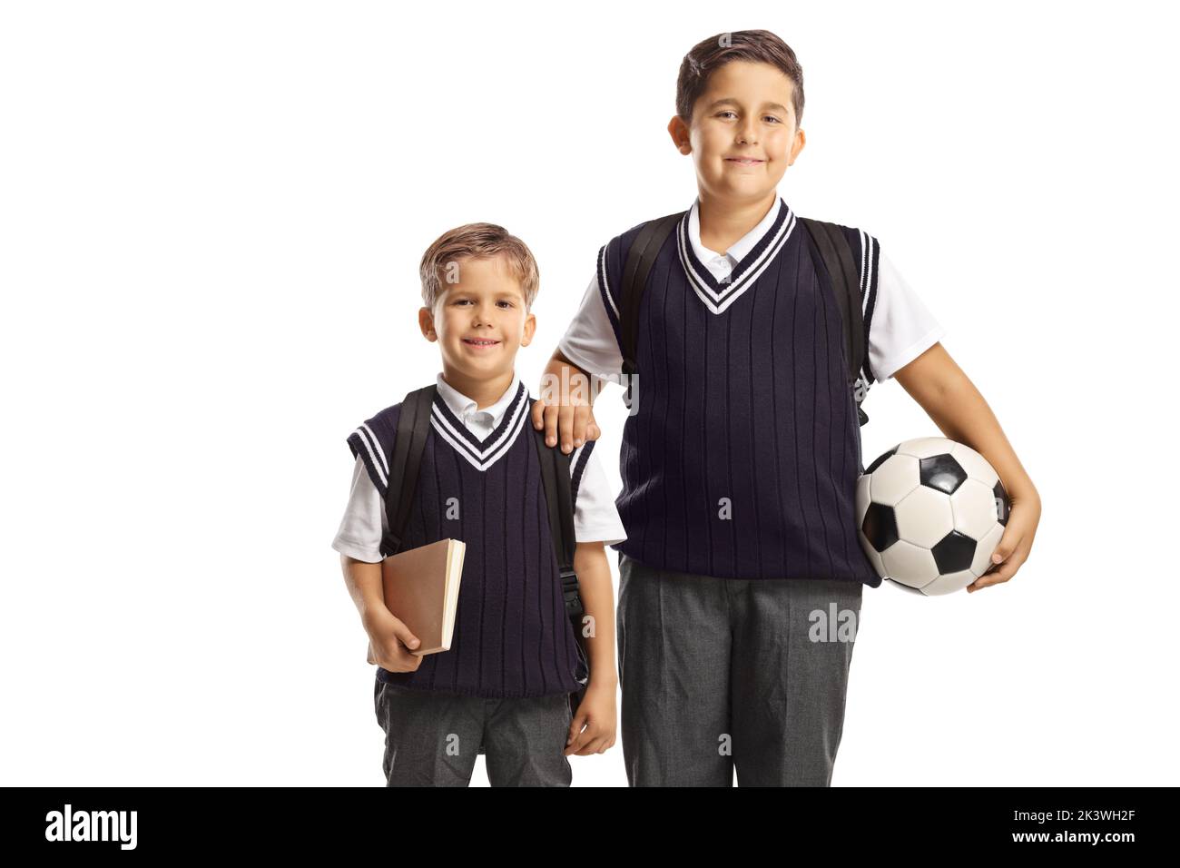 Brüder tragen Schuluniformen und halten einen Fußball isoliert auf weißem Hintergrund Stockfoto