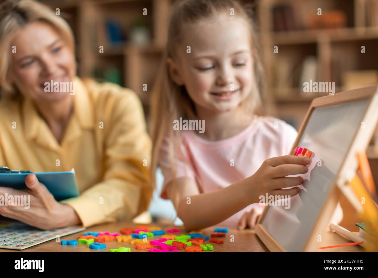 Vorbereitung auf das Schulkonzept. Cleveres kleines Mädchen, das Wort auf dem Whiteboard macht und Alphabet in der Privatklasse studiert Stockfoto