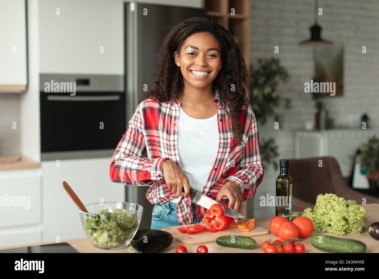 Froh ziemlich tausendjährige afroamerikanische Frau Schneiden Bio-Gemüse und Blick auf die Kamera, genießen Sie das Kochen Stockfoto