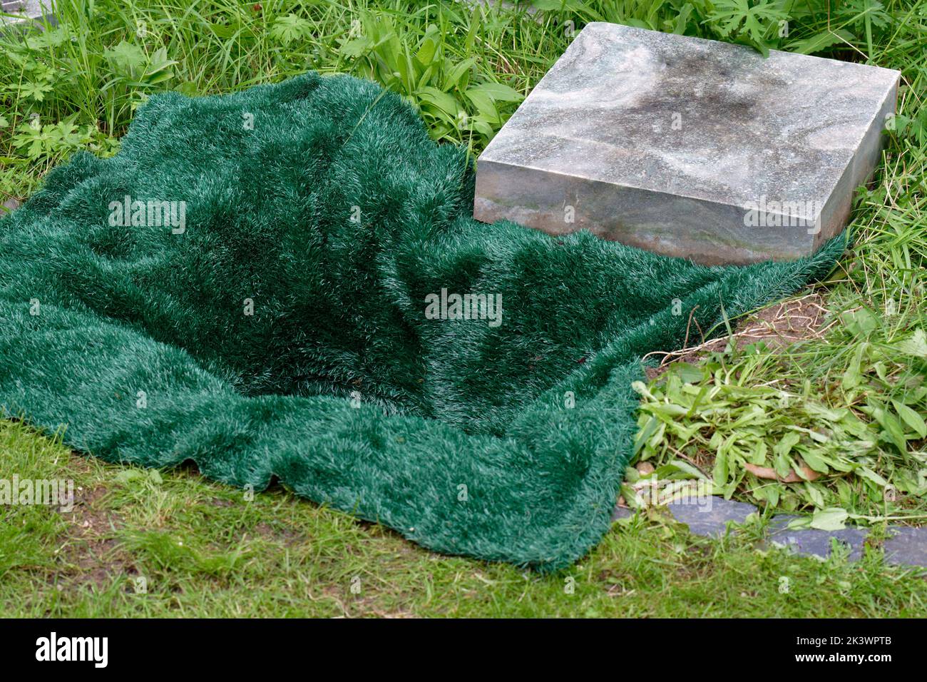 Kleines offenes Grab bedeckt mit einer grünen Matte vor Urnenbestattung auf einem Friedhof Stockfoto