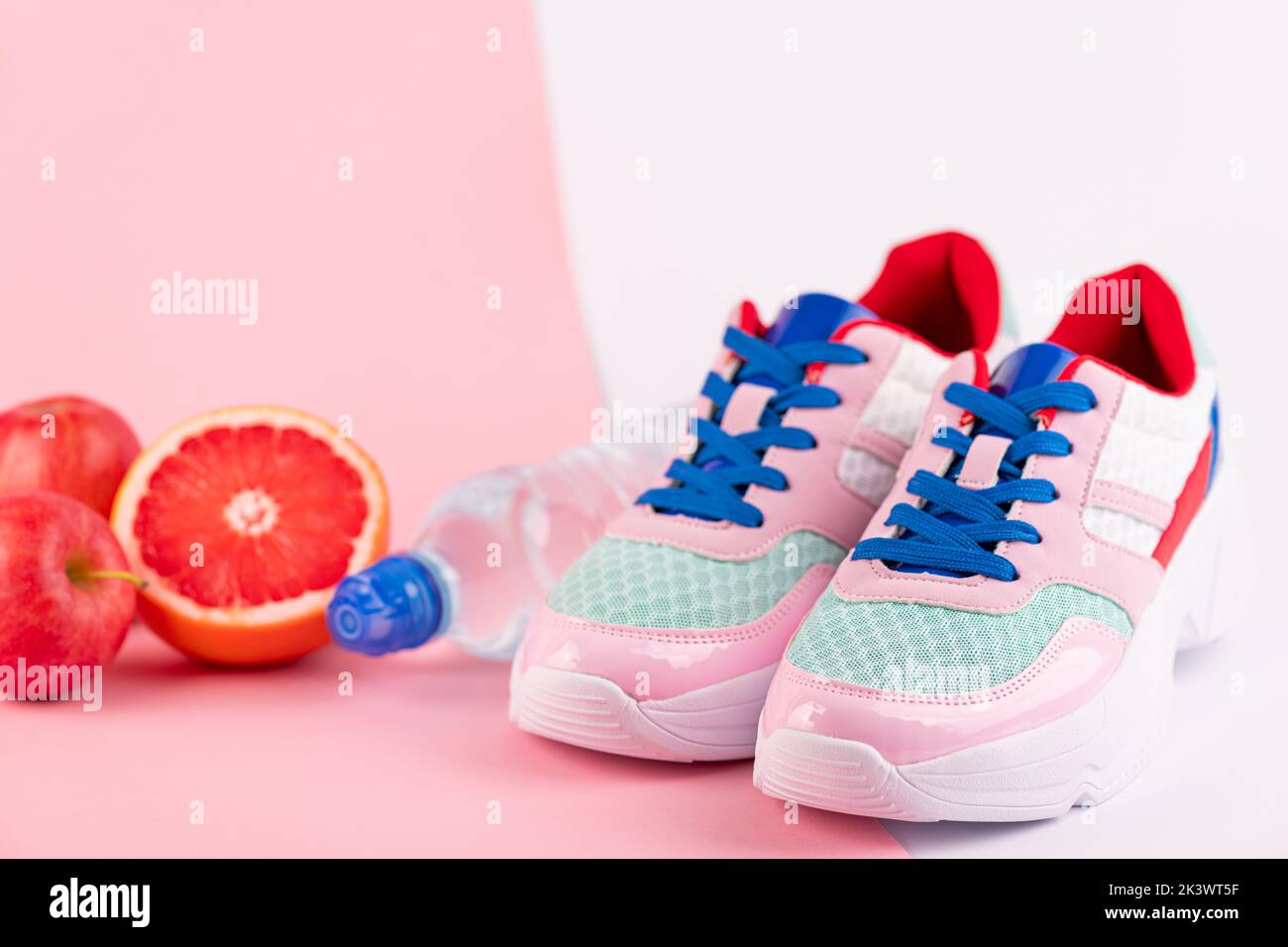 Sportausrüstung Sportschuhe, Flasche Wasser, Zitrusfrüchte auf rosa und weißem Hintergrund. Gesunder Lebensstil, Fitness, Ernährung, Schlankheitskonzept. Trendiges f Stockfoto