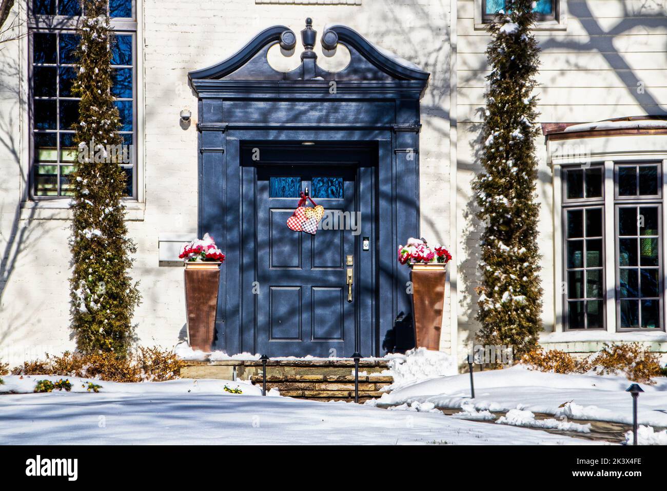 Blaue Haustür mit gebogenen und geschnitzten Rams Kopf Giebel in weißem Haus im Schnee mit Valentine Herzen Dekoration Tür.j Stockfoto
