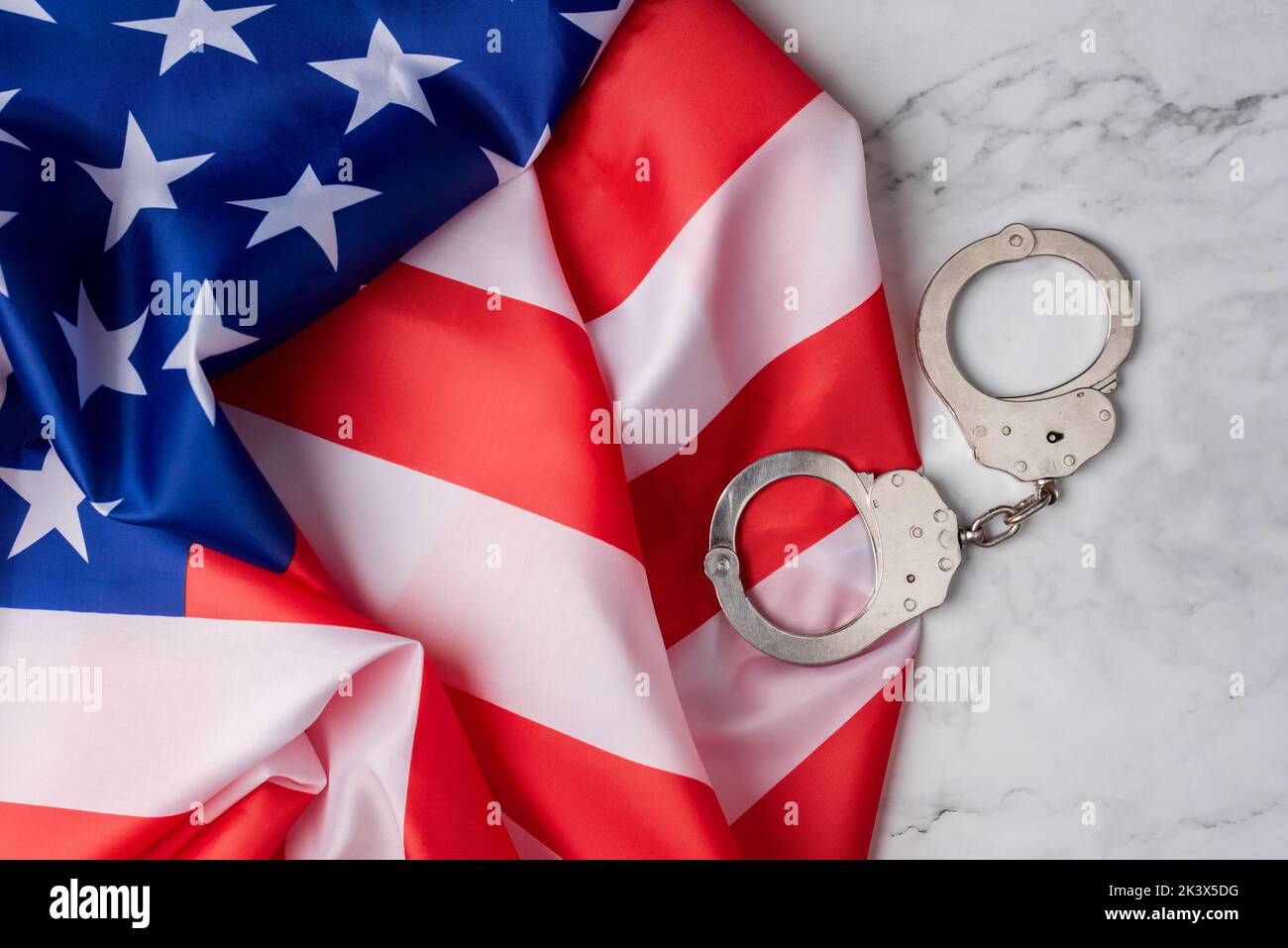 Tapete mit der Flagge der vereinigten Staaten neben Handschellen auf weißem Marmorsockel. Das amerikanische Justizsystem Stockfoto