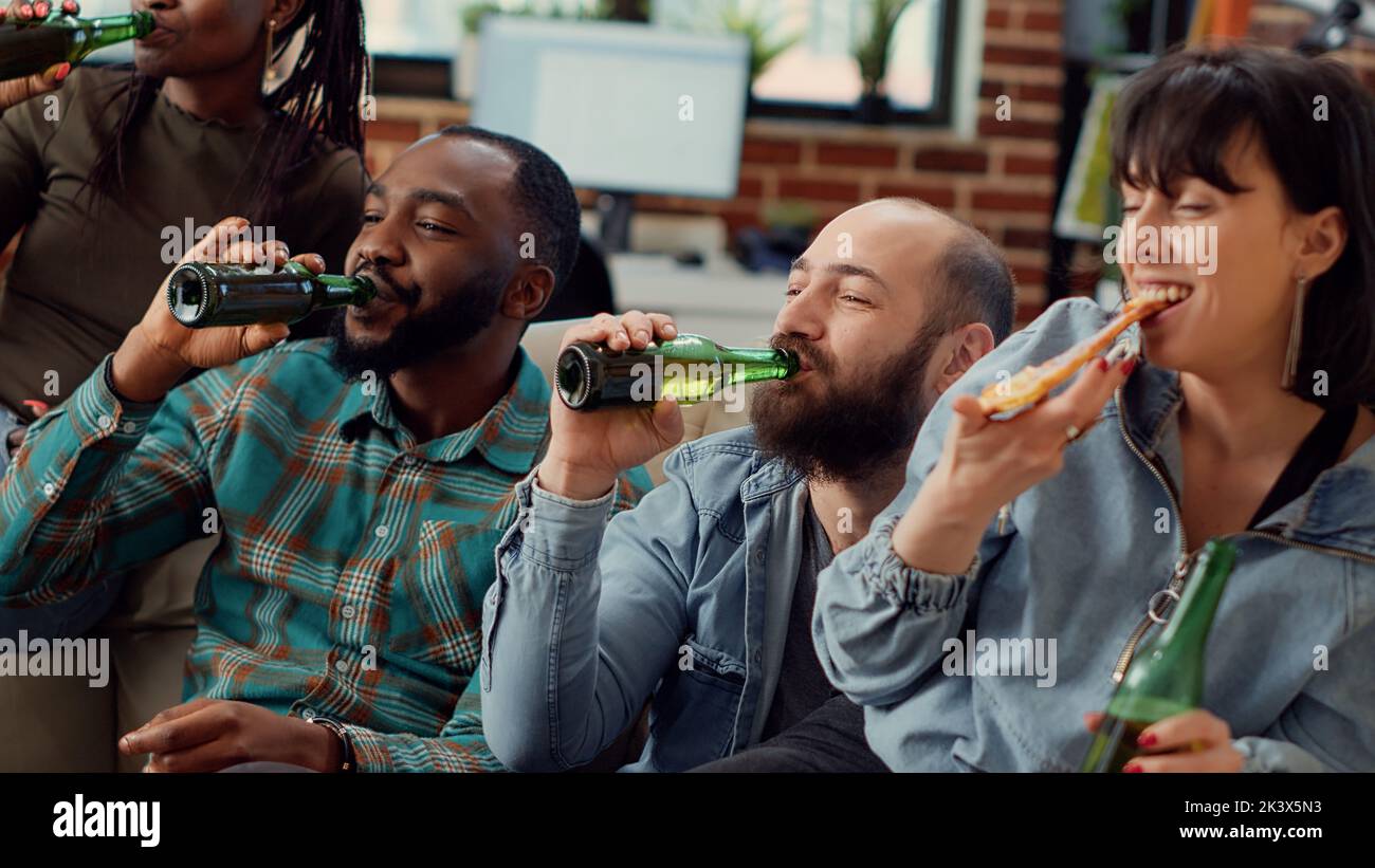 Diverse Freunde, die mit Bierflaschen anstoßen und sich einen Film auf dem fernsehsender ansehen. Spaß am Kinofilm im Fernsehprogramm, Jubel beim geselligen Beisammensein. Handgeführte Aufnahme. Stockfoto