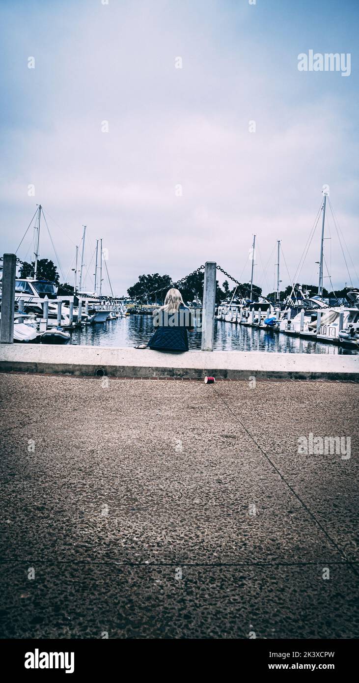 Eine vertikale Aufnahme einer Frau, die in einem Hafen voller Boote unter bewölktem Himmel sitzt Stockfoto