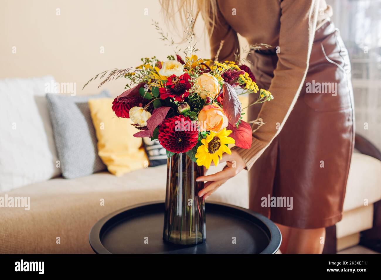 Frau stellt Vase mit Blumenstrauß von Sonnenblumen Dahlien Rosen und Zinnia Blumen auf den Tisch. Innenausstattung und Herbstdekor zu Hause. Stockfoto
