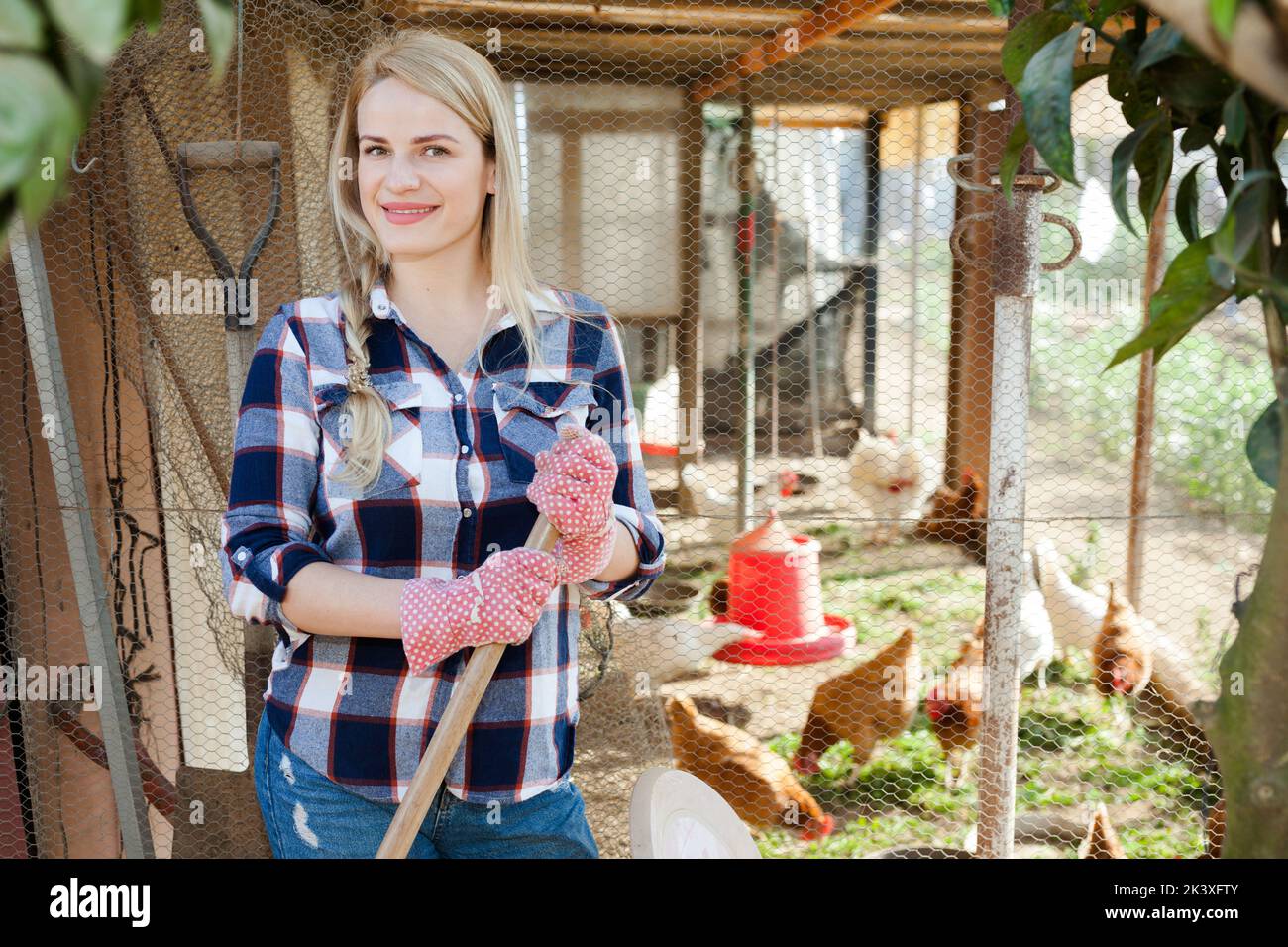 Lächelnde junge, professionelle Bäuerin, die im Hühnerstall steht Stockfoto