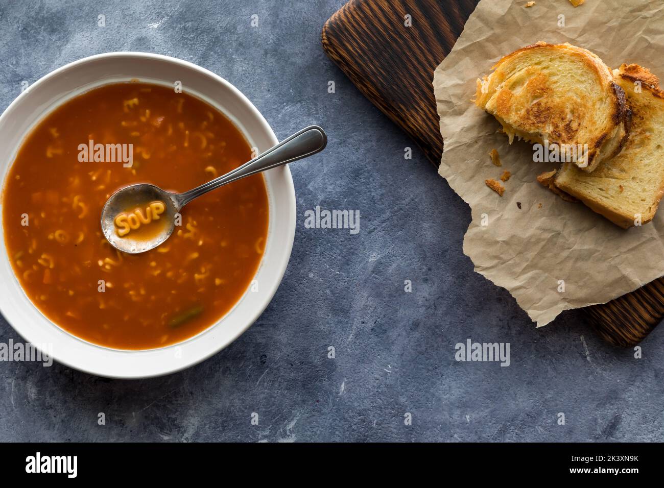 Buchstabensuppe mit dem Wort Suppe im Löffel serviert mit gegrilltem Käse. Stockfoto