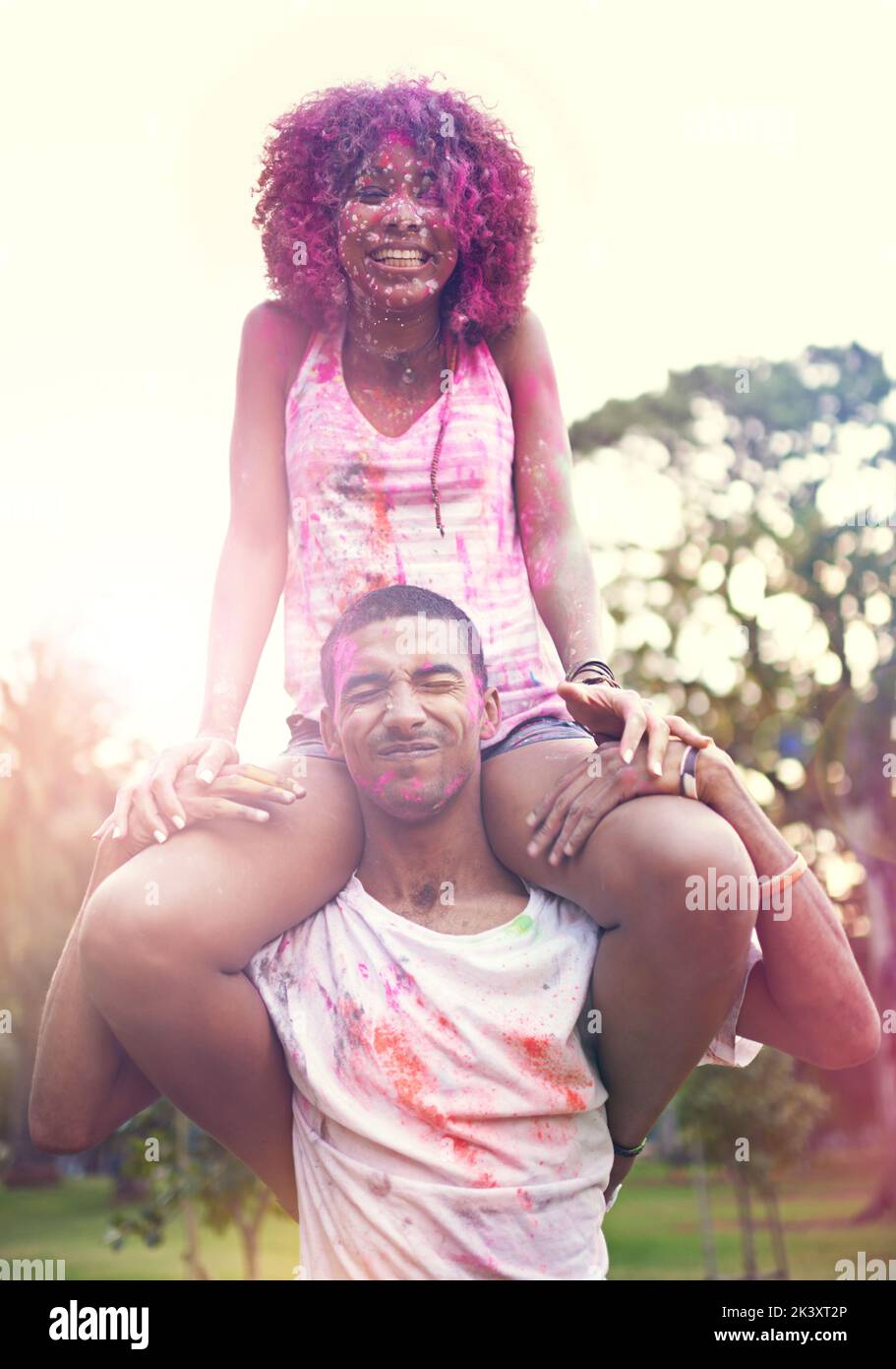 Ein junger Mann, der eine Frau auf seinen Schultern auf einem Farbfestival trägt. Stockfoto