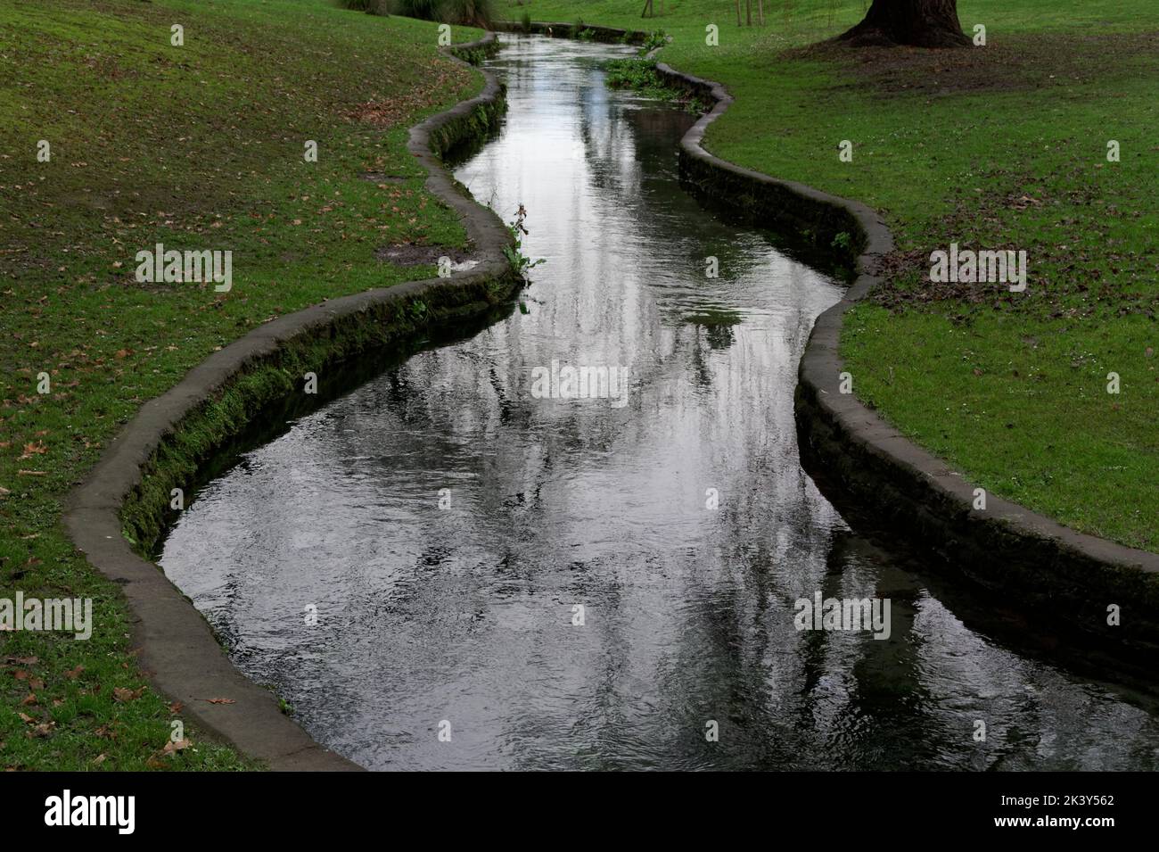 Ein Bach wurde von Betonseiten eingedämmt, um durch einen öffentlichen Park zu wandern Stockfoto