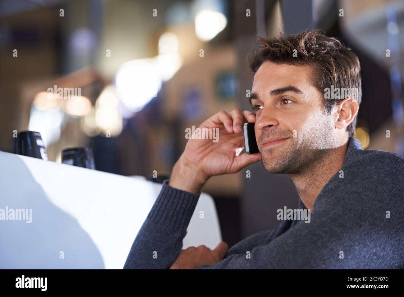 Einen Freund für Kaffee anrufen. Ein junger Mann spricht auf seinem Handy, während er in einem Café sitzt. Stockfoto