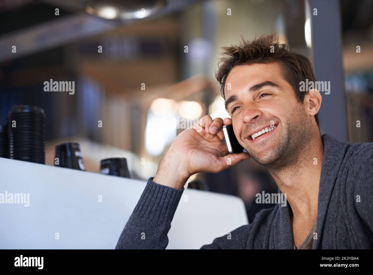 Einen Freund für Kaffee anrufen. Ein junger Mann spricht auf seinem Handy, während er in einem Café sitzt. Stockfoto