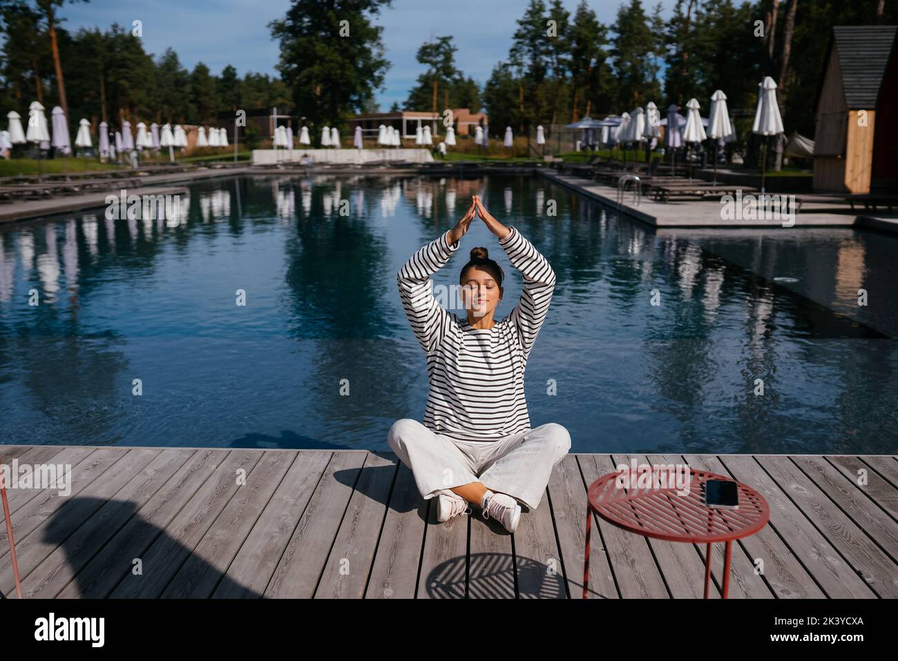 Junge Fitness-Frau, die ihren morgendlichen Yoga in der Nähe des Pools macht Stockfoto