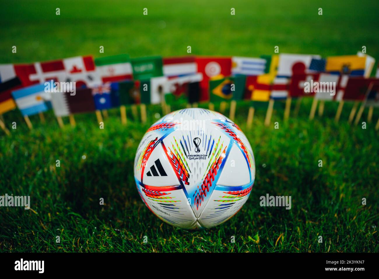 KATAR, DOHA, 18. JULI 2022: FIFA Fußball-Weltmeisterschaft Katar 2022 Hintergrund. Offizieller Adidas Ball auf grünem Gras und Nationalflaggen aller 32 Teilnehmer. Stockfoto