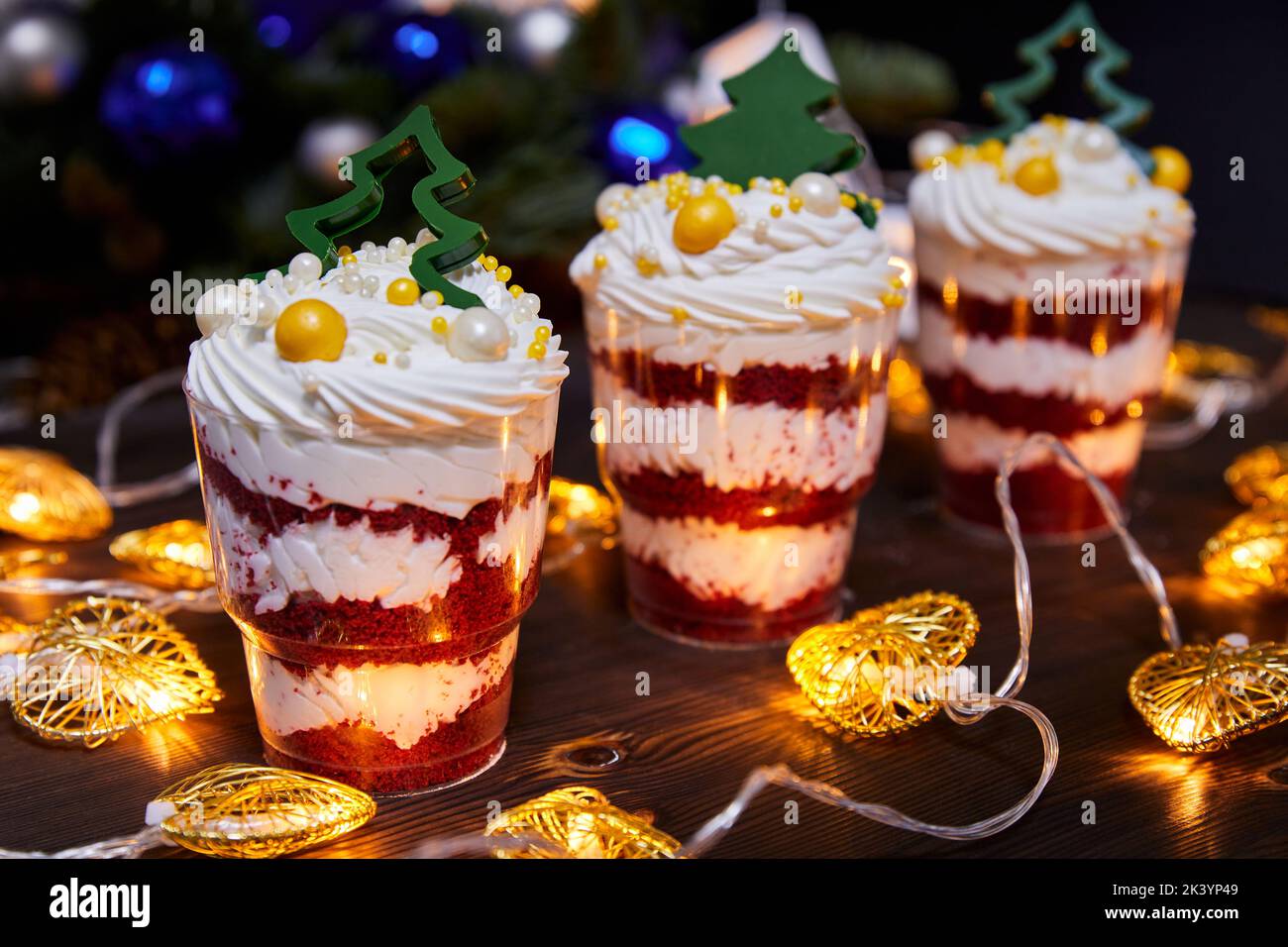 Weihnachts-Kleinigkeiten in Tassen als Dessert, verziert mit Schokoladen-Neujahr-Bäumen, für einen festlichen Tisch auf dem Hintergrund glühender Girlanden Stockfoto