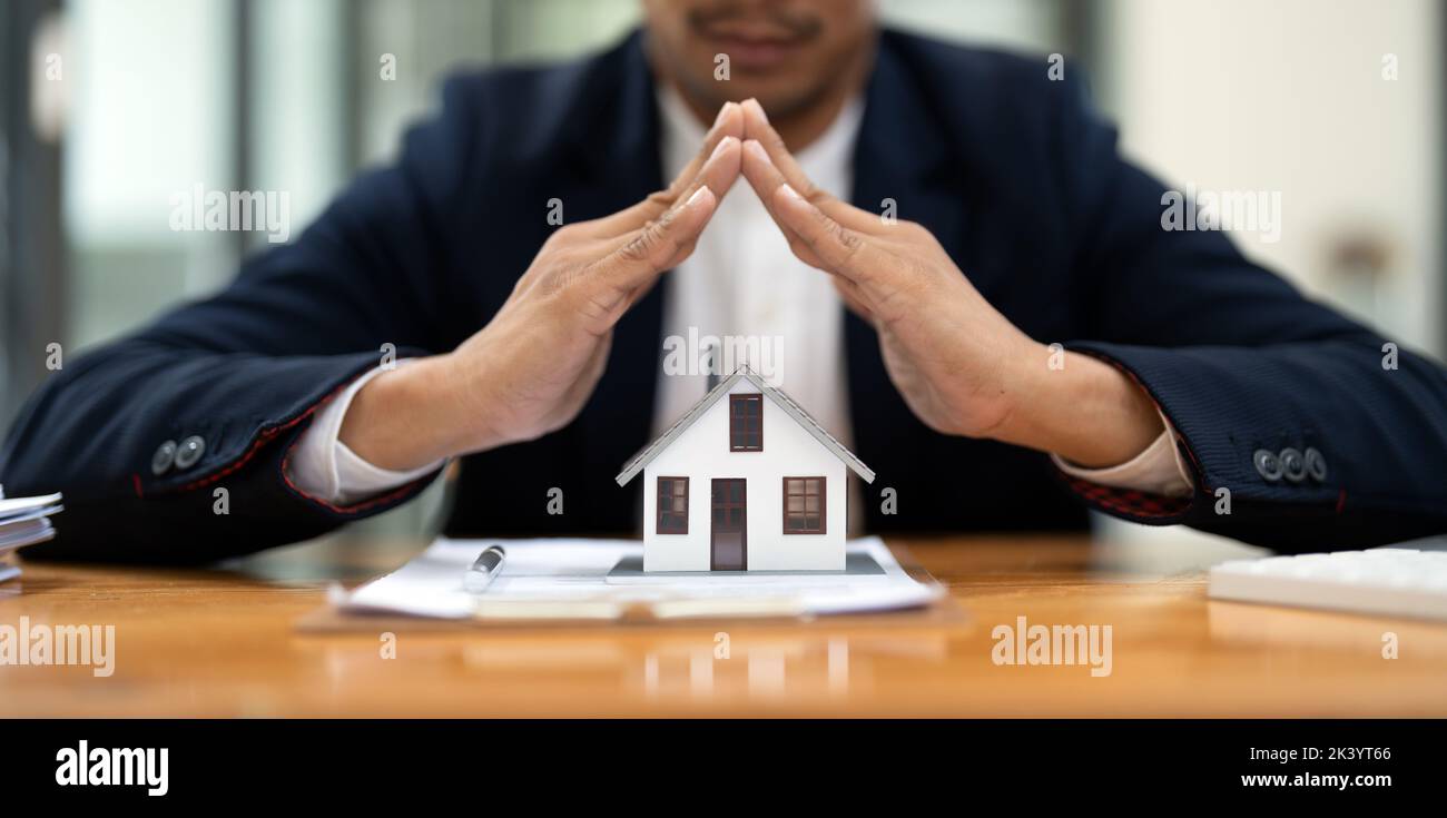 Immobilienkonzept, Geschäftsmann Holding schützen Haus Modell. Sachversicherung und Sicherheitskonzept. Schützende Geste des Menschen und Symbol des Hauses. Stockfoto