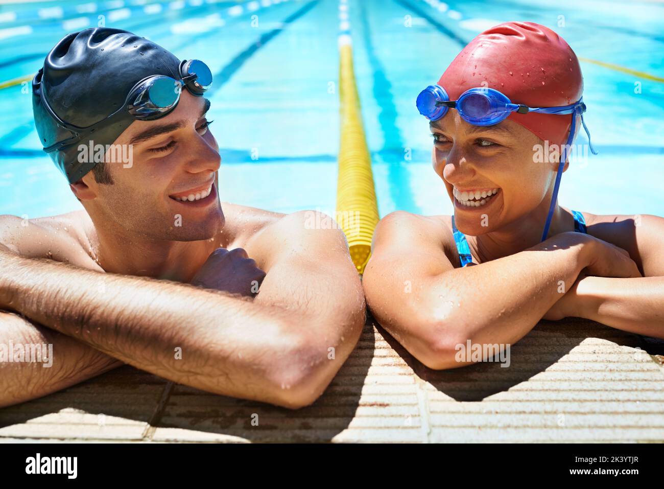 Der perfekte Tag zum Schwimmen. Zwei junge Schwimmer lächeln die Kamera mit einem Lächeln an, während sie im Pool stehen. Stockfoto