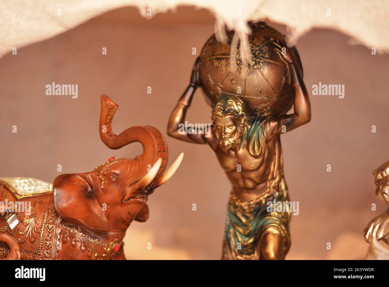 Bronzestatue mit einem Mann, der den Erdball hinter sich trägt, und einem hölzernen Elefanten im Profil. Der Mann ist Atlas Stockfoto