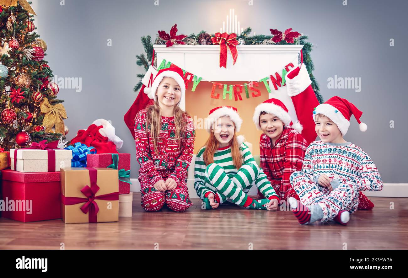 Gruppe von Kindern, die am Weihnachtsmorgen drinnen auf dem Boden sitzen. Stockfoto