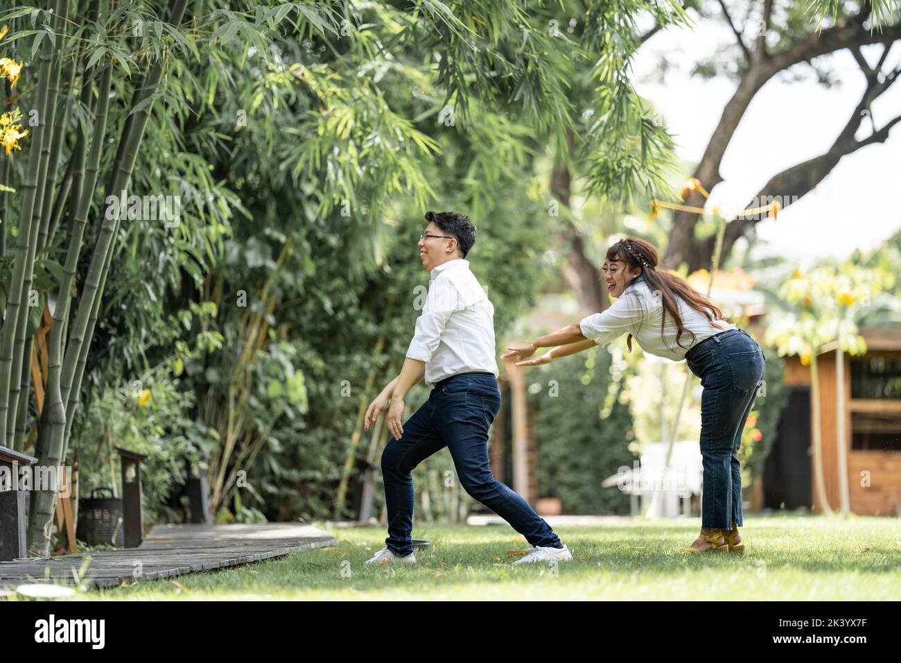 Asiatische Mann und Frau machen ein Foto vor der Hochzeit mit Frau, die seine Schulter greift und den Mann im Garten versteifet. Stockfoto