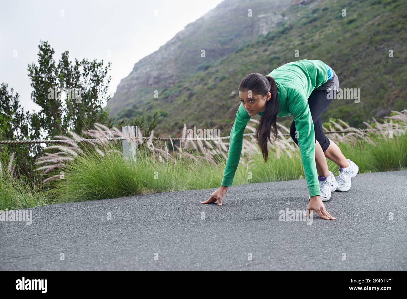 Bereit, diese Straße zu ihrer eigenen zu machen... Eine junge Frau, die auf der Straße hockend, um zu laufen. Stockfoto