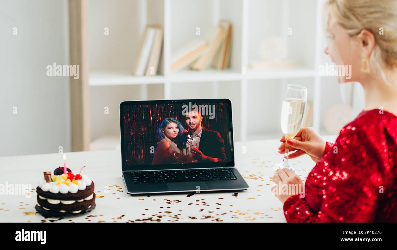 Virtuelle Party. Weihnachtsgrüße. Online-Verbindung. Festliche Frau mit Glas Champagner Feiertagskuchen immer Gratzen von Paar auf Laptop in Licht Stockfoto