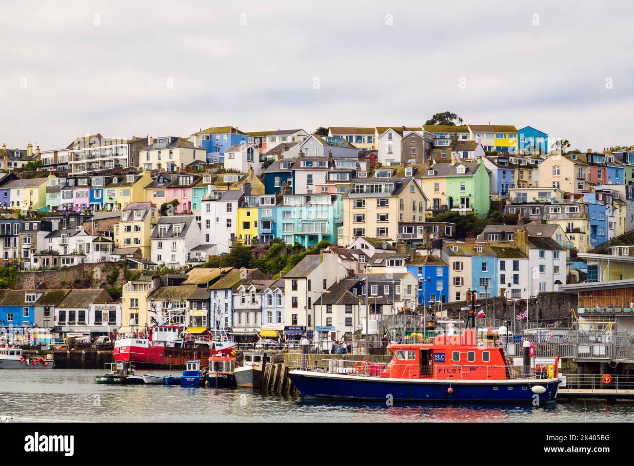 Farbenfrohe Häuser auf dem Hügel mit Blick auf den inneren Hafen und einem Steuerboot, das am Kai andockt. Brixham, Devon, England, Großbritannien Stockfoto