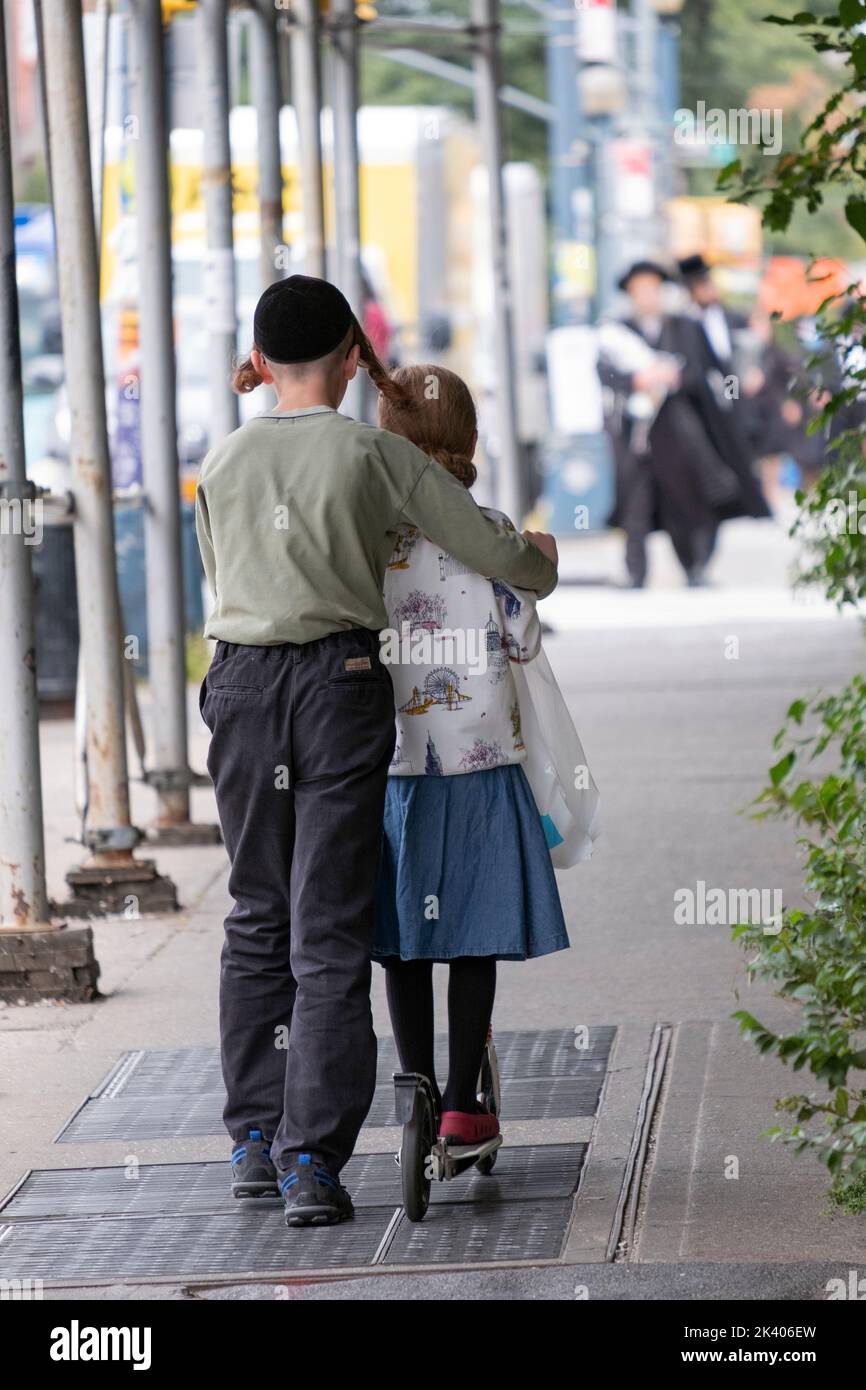 Ein anonymer chassidischer jüdischer Teenager lehrt seine Schwester, wie man einen Roller fährt. Auf der Lee Avenue in Williamsburg, Brooklyn, New York. Stockfoto