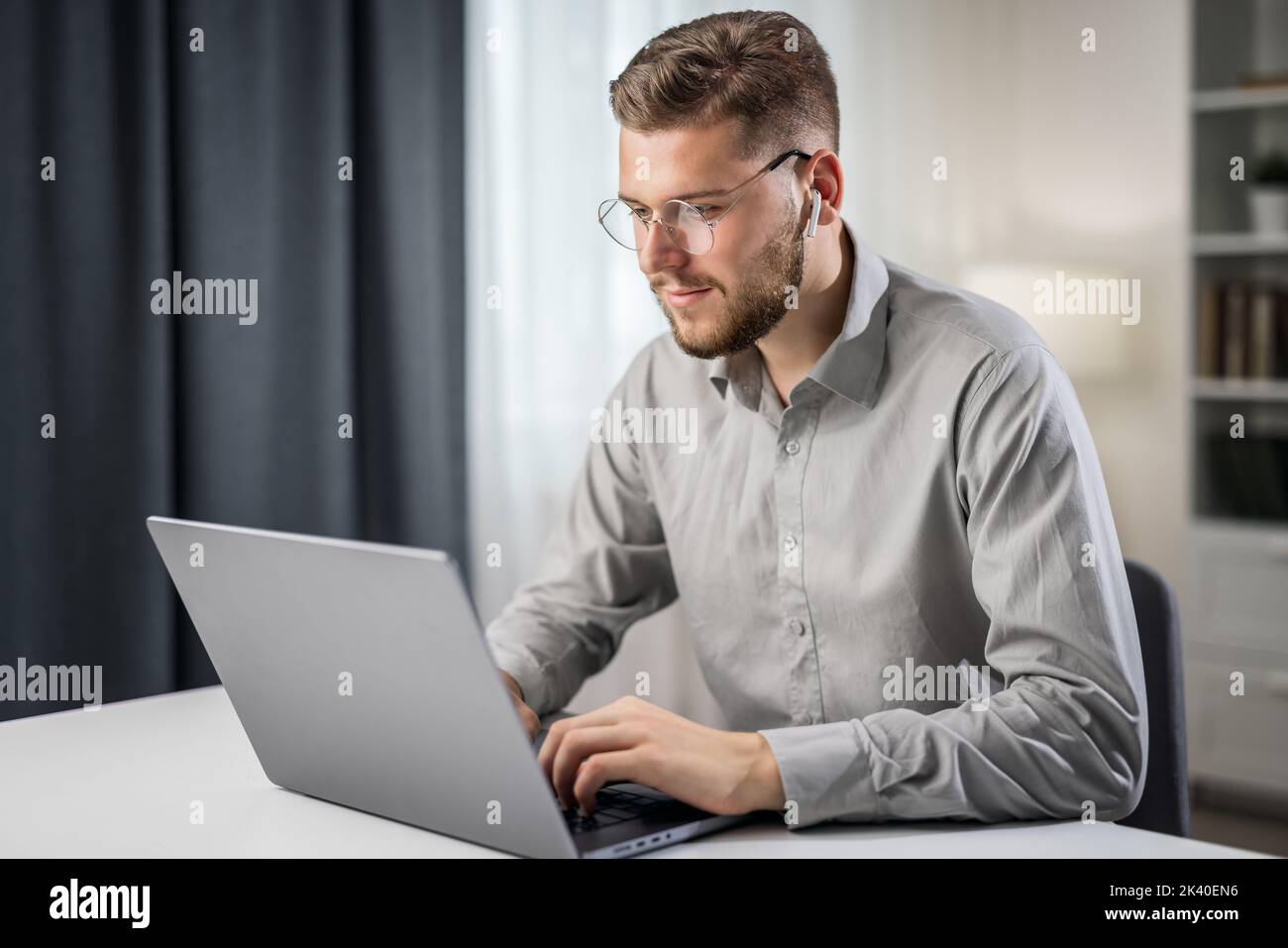 Schöner Mann in grauem Hemd, der von zu Hause aus am Laptop codiert und fernab arbeitet, um Code zu schreiben Stockfoto